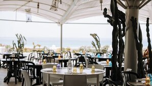Un espace extérieur aménagé pour les repas, avec des tables rondes, des chaises noires et une vue sur la mer.