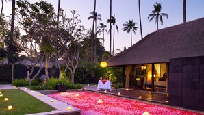 A resort with a thatched-roof building, a flower-adorned pathway, and lush greenery.