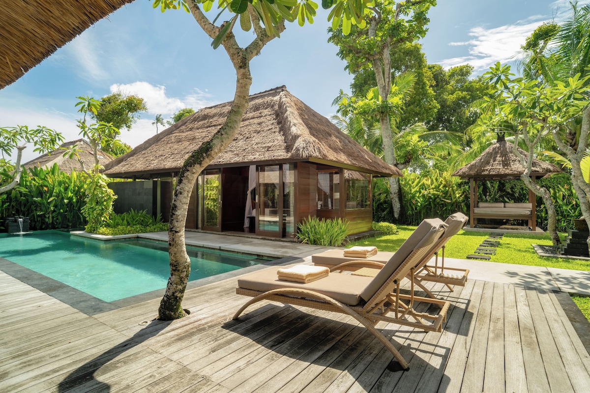 A poolside area with a thatched-roof structure, lounge chairs, and a clear view of the pool.
