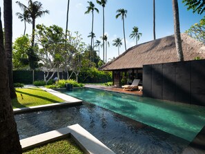 Una piscina con una estructura de techo de paja, rodeada de palmeras y follaje.