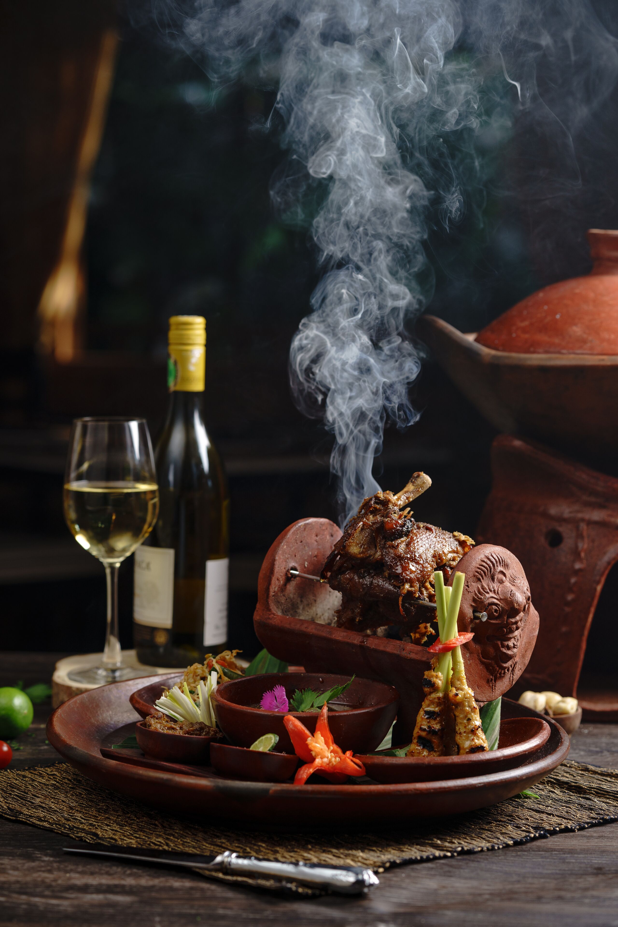 Una olla de barro tradicional con un guiso asado y una botella de vino sobre una mesa.