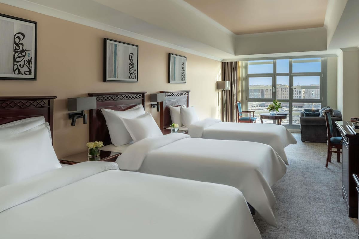 A hotel room with three beds, a desk, a chair, and a view of the city.
