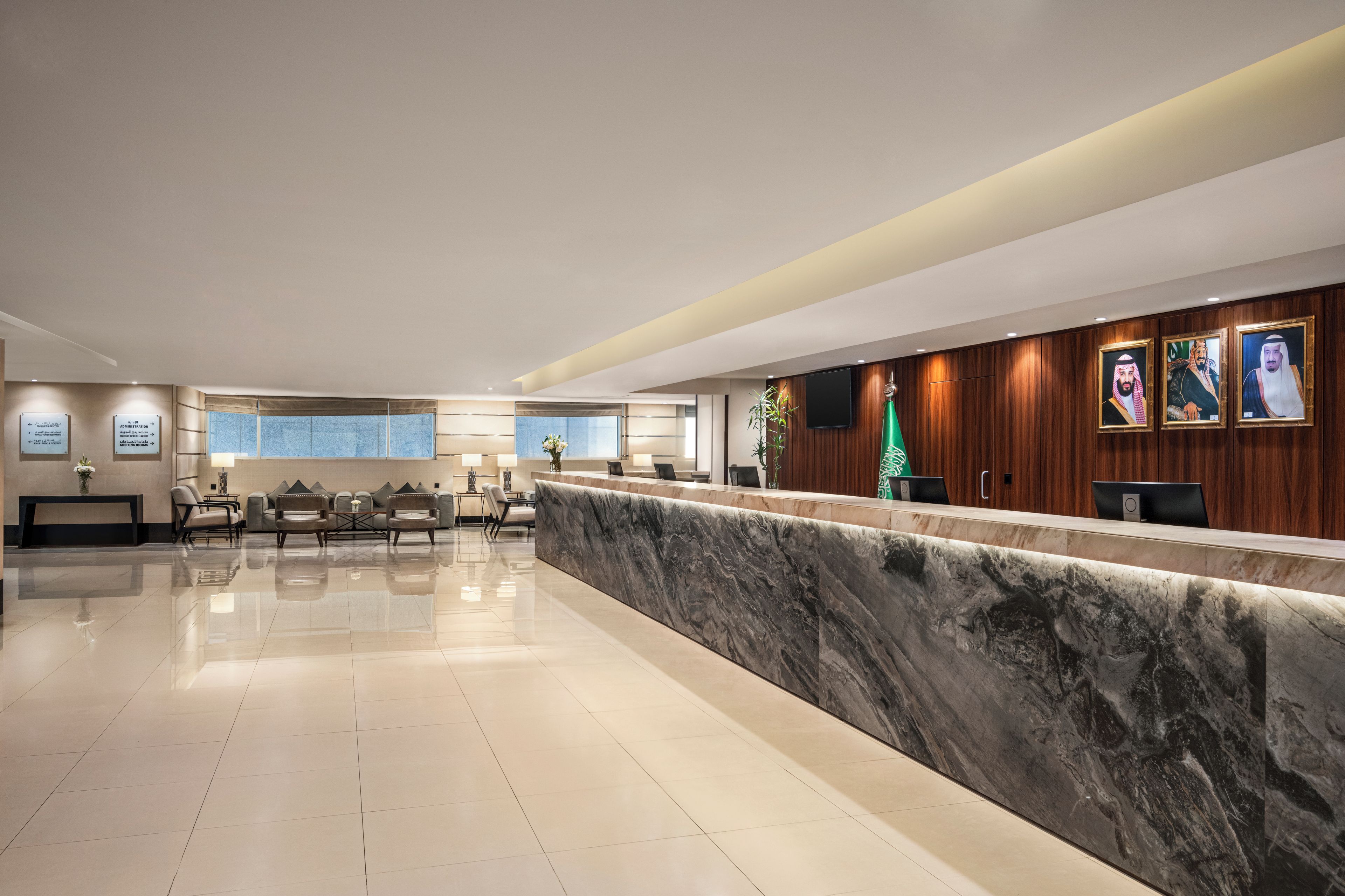 A hotel lobby with a reception desk, seating area, and directional signs.