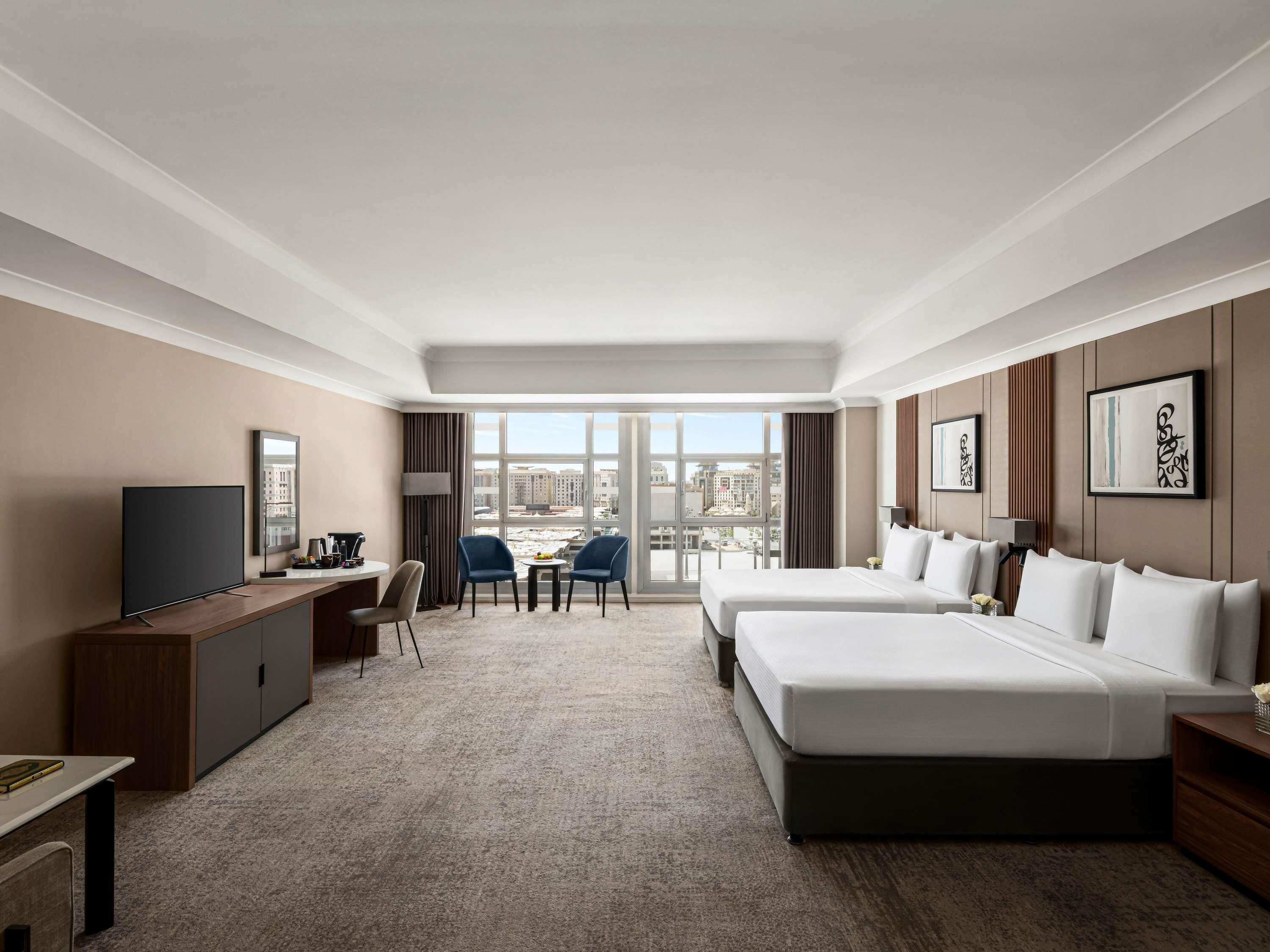 A hotel room with a large bed, a desk, a TV, and a view of the city.