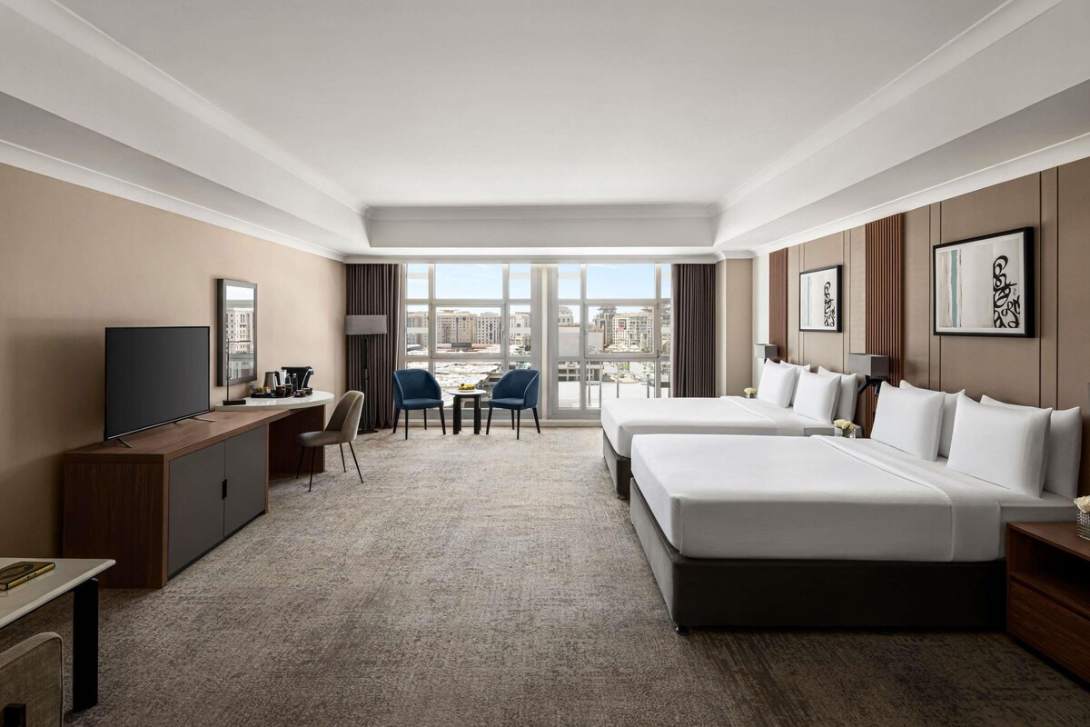 Habitación de hotel con una cama grande, un escritorio, un televisor y vistas a la ciudad.