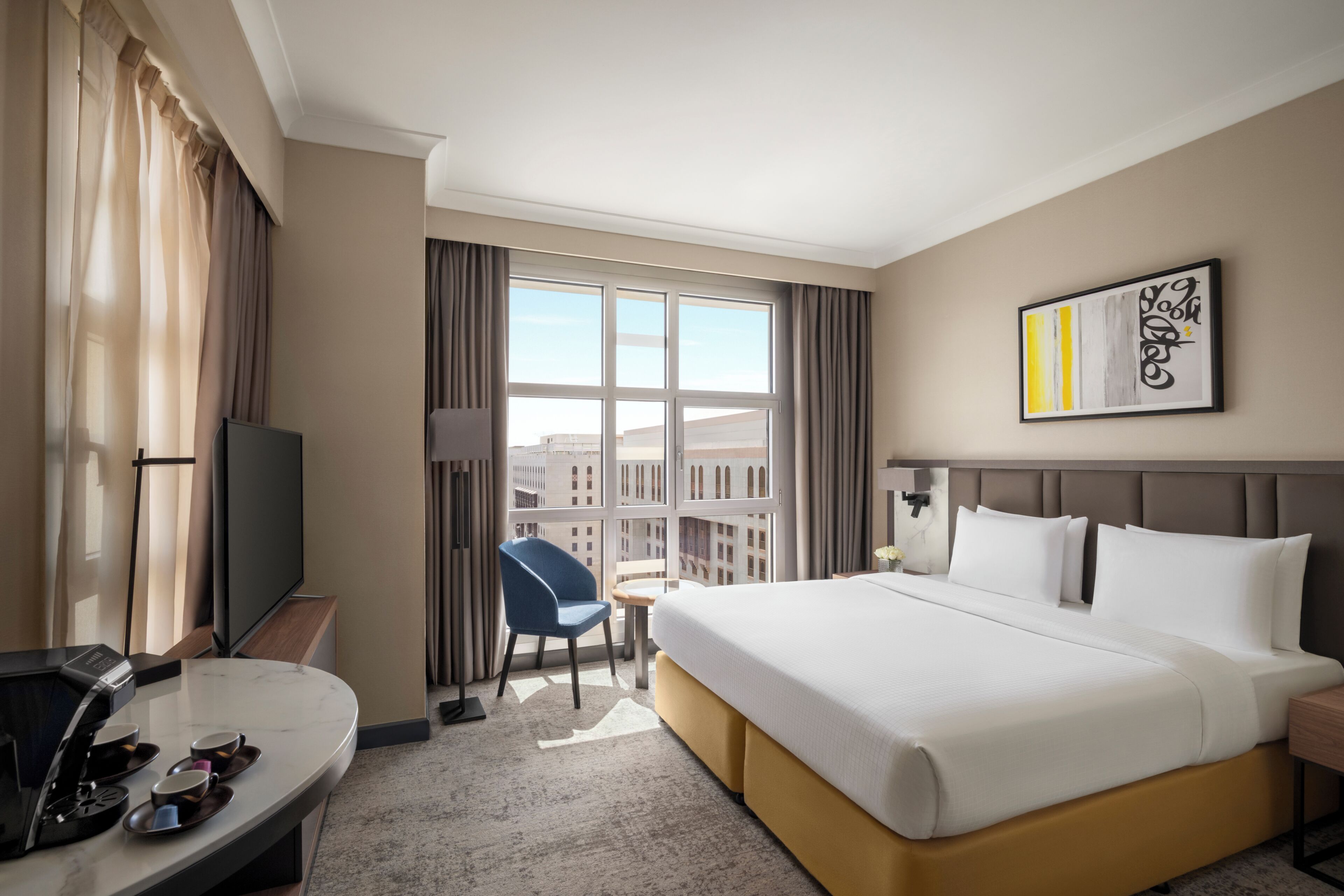 Habitación de hotel con una cama grande, un escritorio con cafetera, una silla y un televisor.