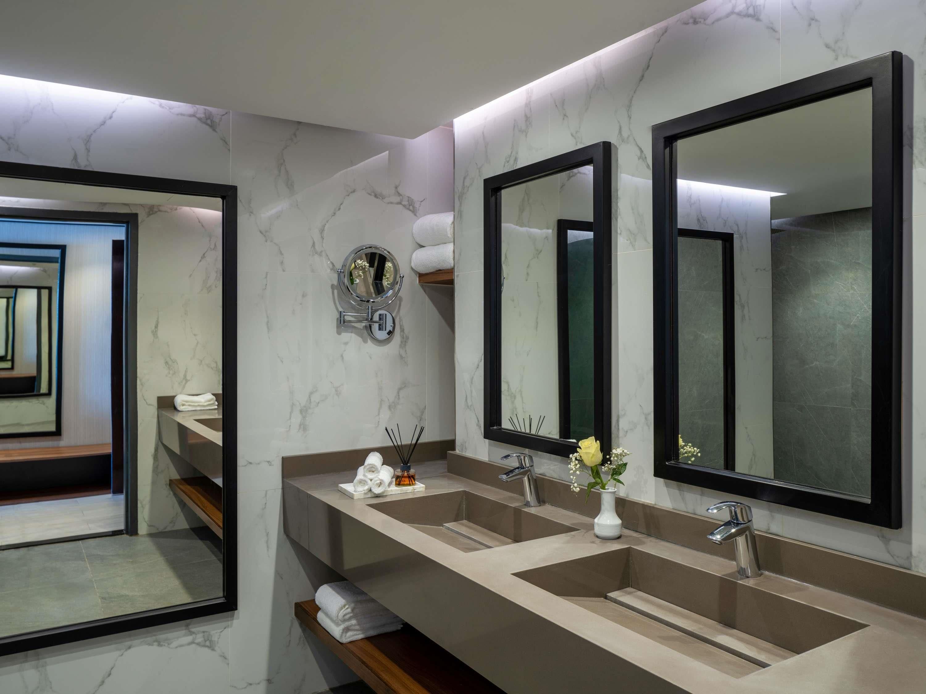 Une salle de bain moderne avec deux lavabos, de grands miroirs et un mur en marbre.