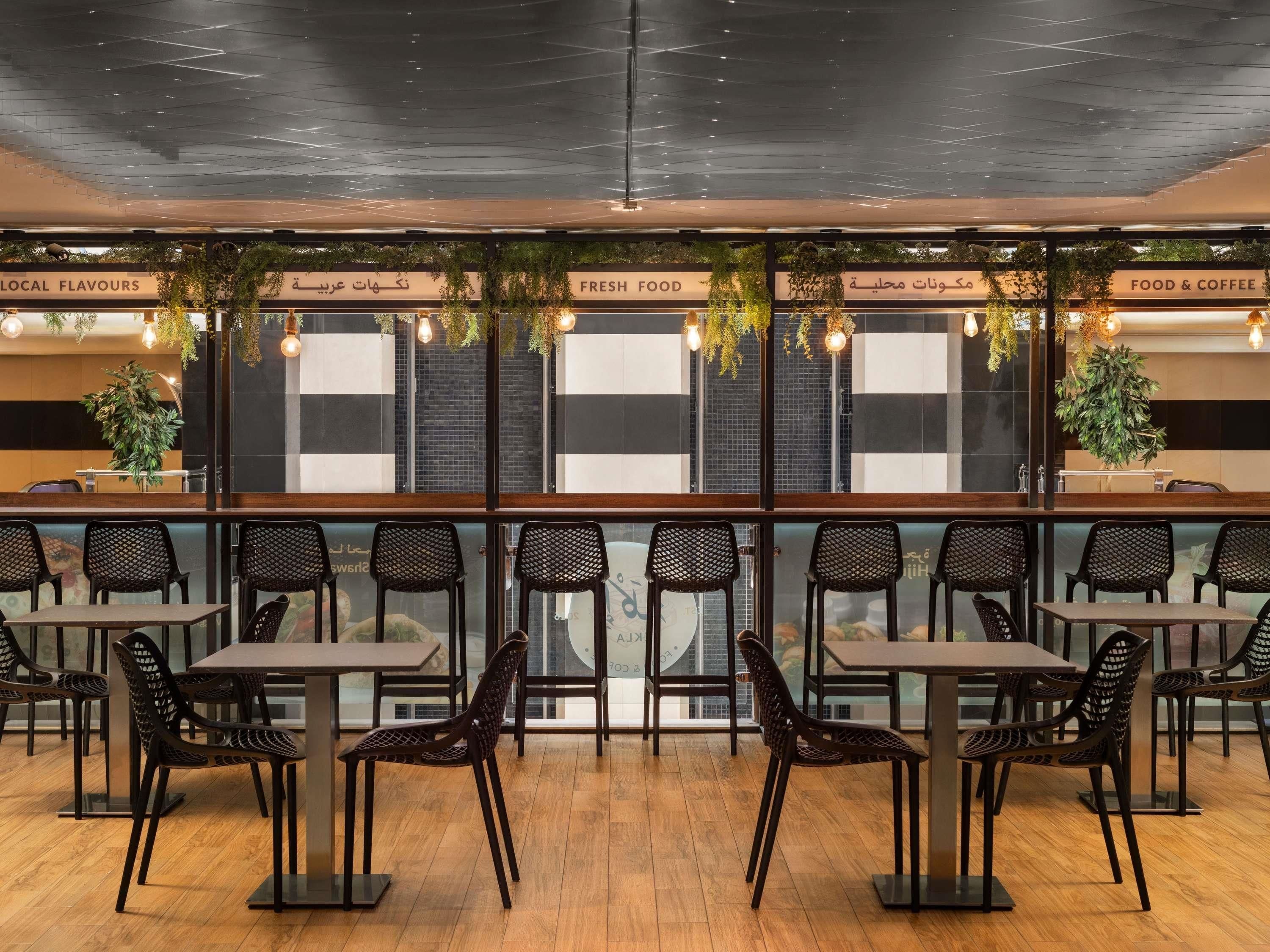 Ein Restaurant mit modernem Ambiente, das schwarze Mesh-Stühle, Holztische und eine Decke mit freiliegenden Balken zeigt.