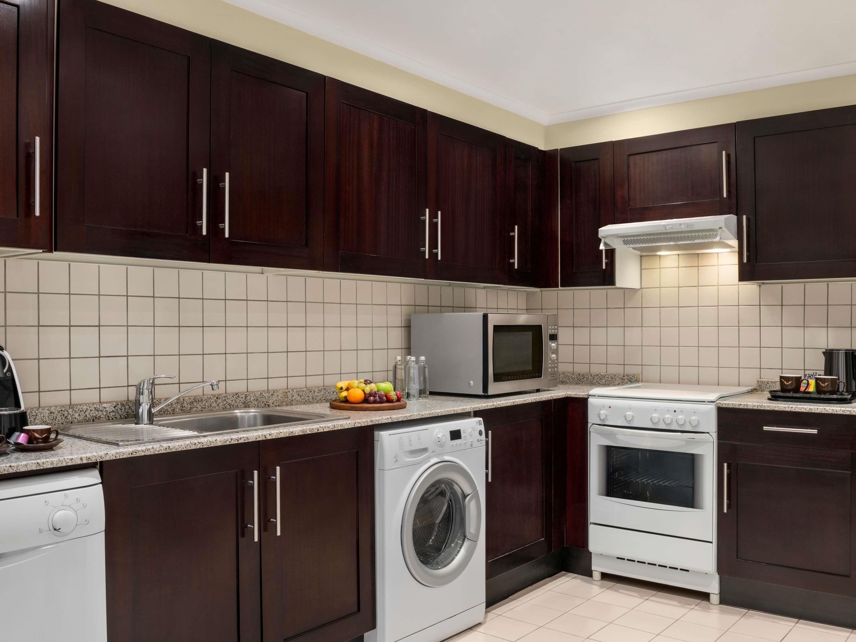 A modern kitchen with dark wooden cabinets, a stainless steel sink, a microwave, a washing machine, and a stove.