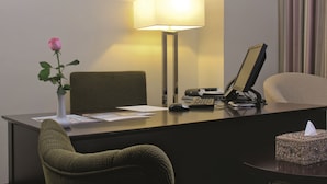 A hotel reception desk with a vase of flowers, a desk lamp, a computer, and a chair.