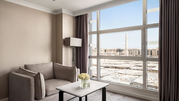 A room with a sofa, a small table with a vase, a TV, and a large window with curtains.