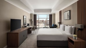 A hotel room with a large bed, a desk, a television, and a view of the city.
