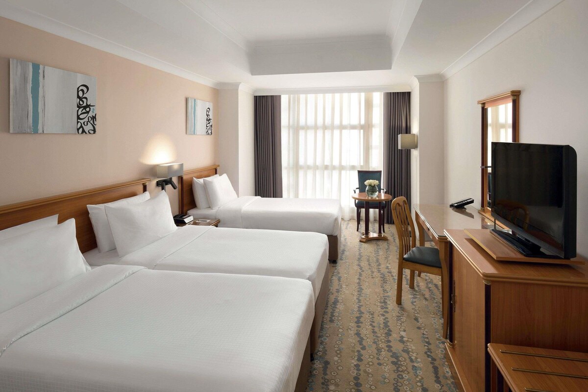 Habitación de hotel con dos camas, un escritorio con silla, un televisor y una ventana con cortinas.