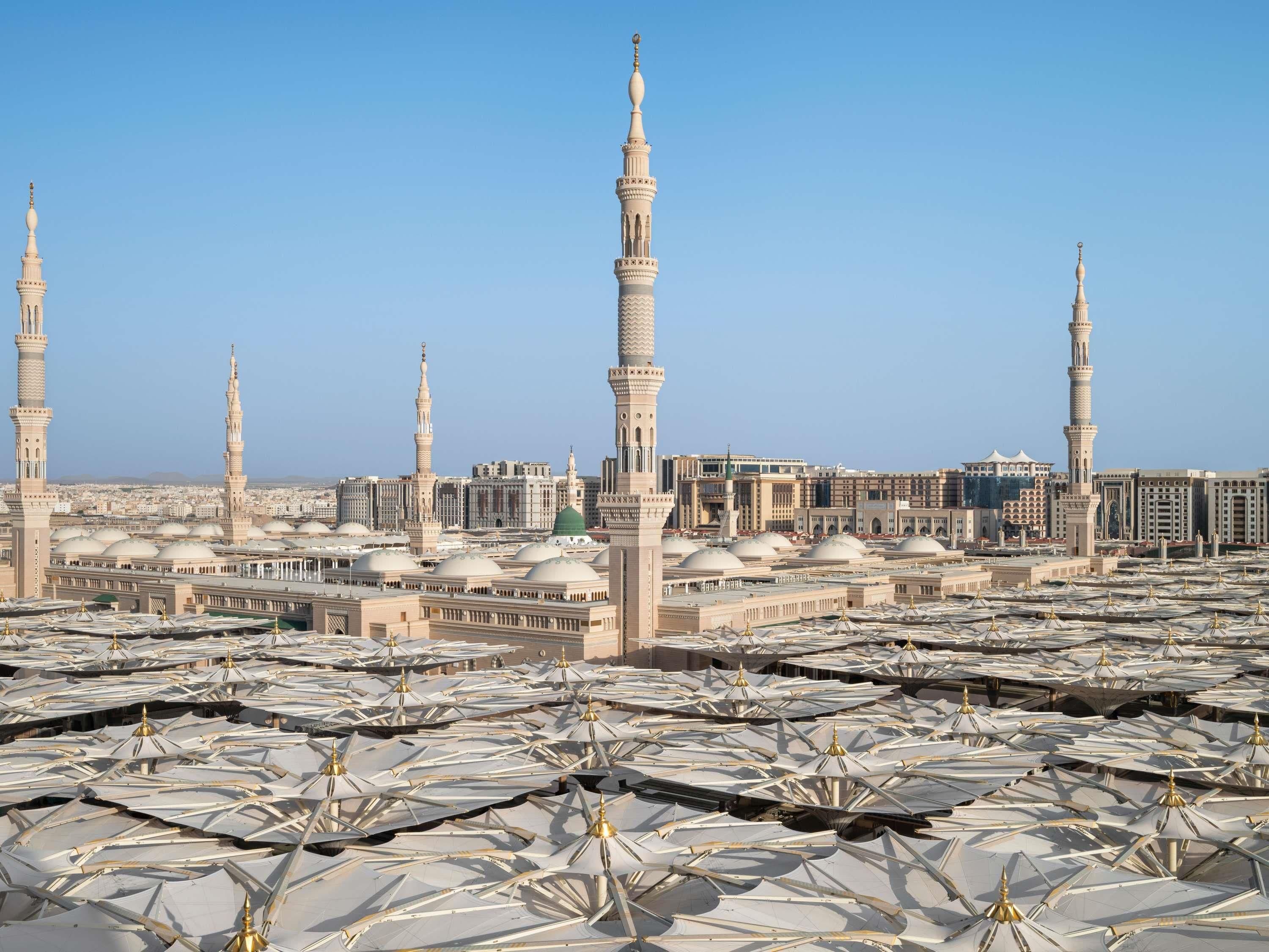 A mosque with multiple minarets and a large courtyard with numerous white canopies.