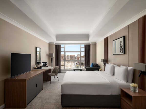 Habitación de hotel con una cama grande, un escritorio, un televisor, una silla y vistas a la ciudad.