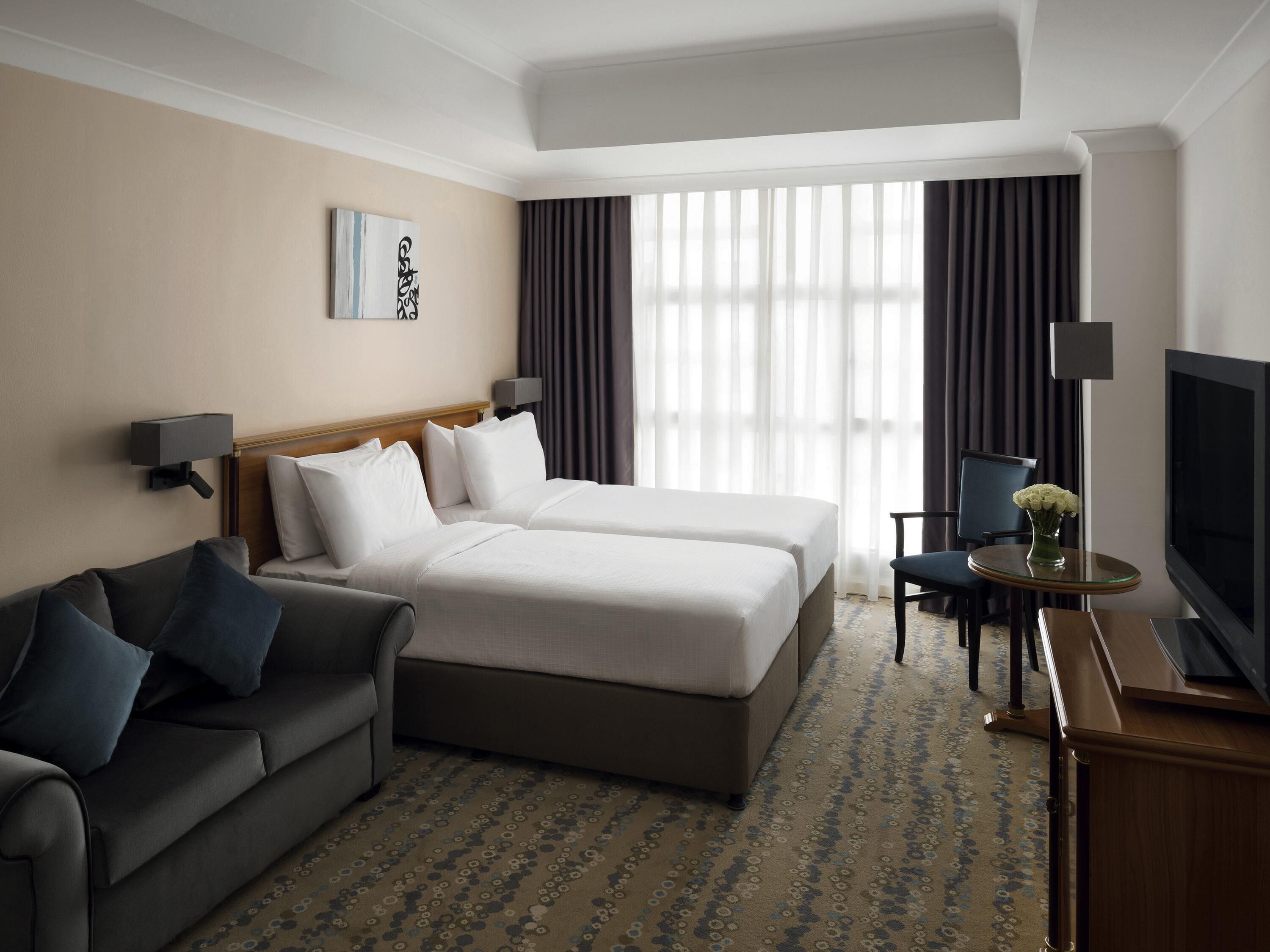 A hotel room with a bed, a sofa, a TV, and a desk with a lamp.