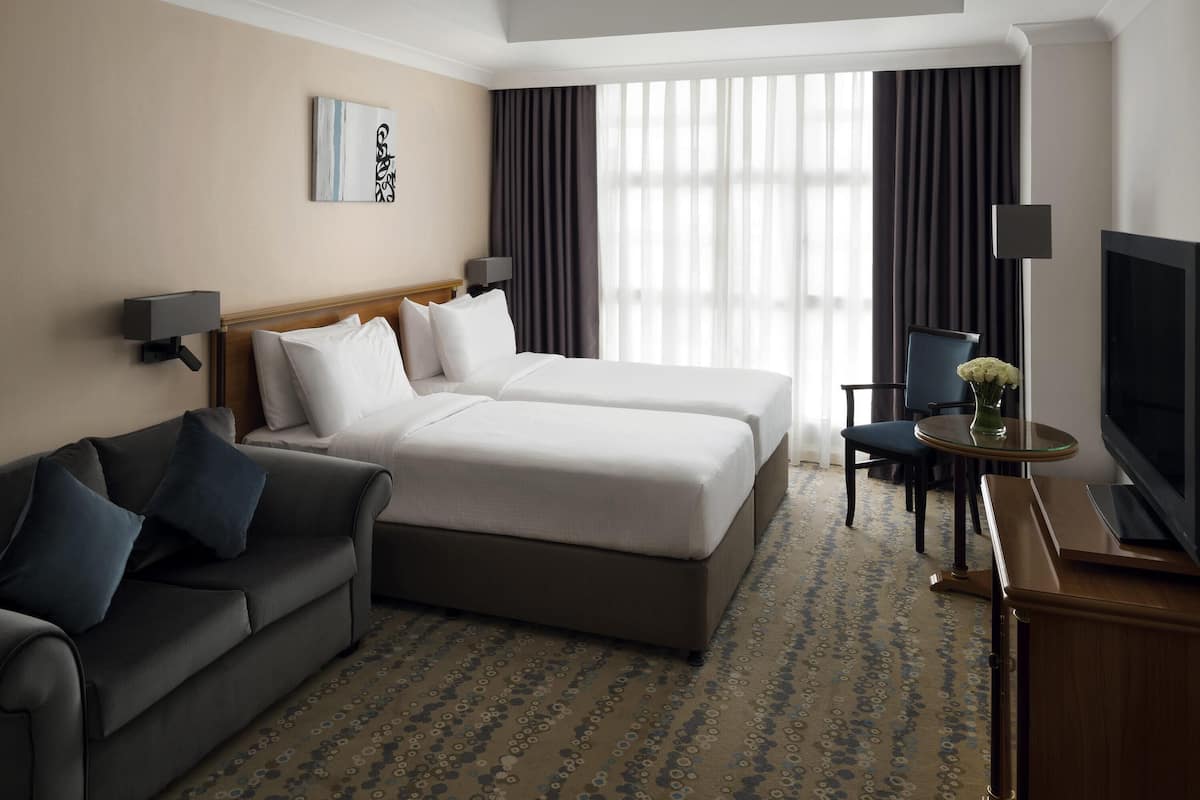A hotel room with a bed, a sofa, a TV, and a desk with a lamp.