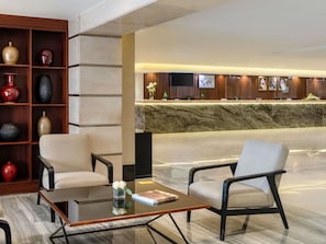 Un hall d’entrée avec un comptoir de réception, deux fauteuils, une table basse et une bibliothèque agrémentée d’objets décoratifs.