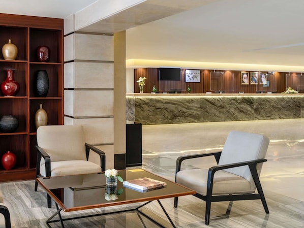 Un hall amb una recepció, dos butaques, una taula de cafè i una estanteria amb elements decoratius.