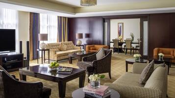 A hotel living room with a television, sofas, a dining area, and a chandelier.