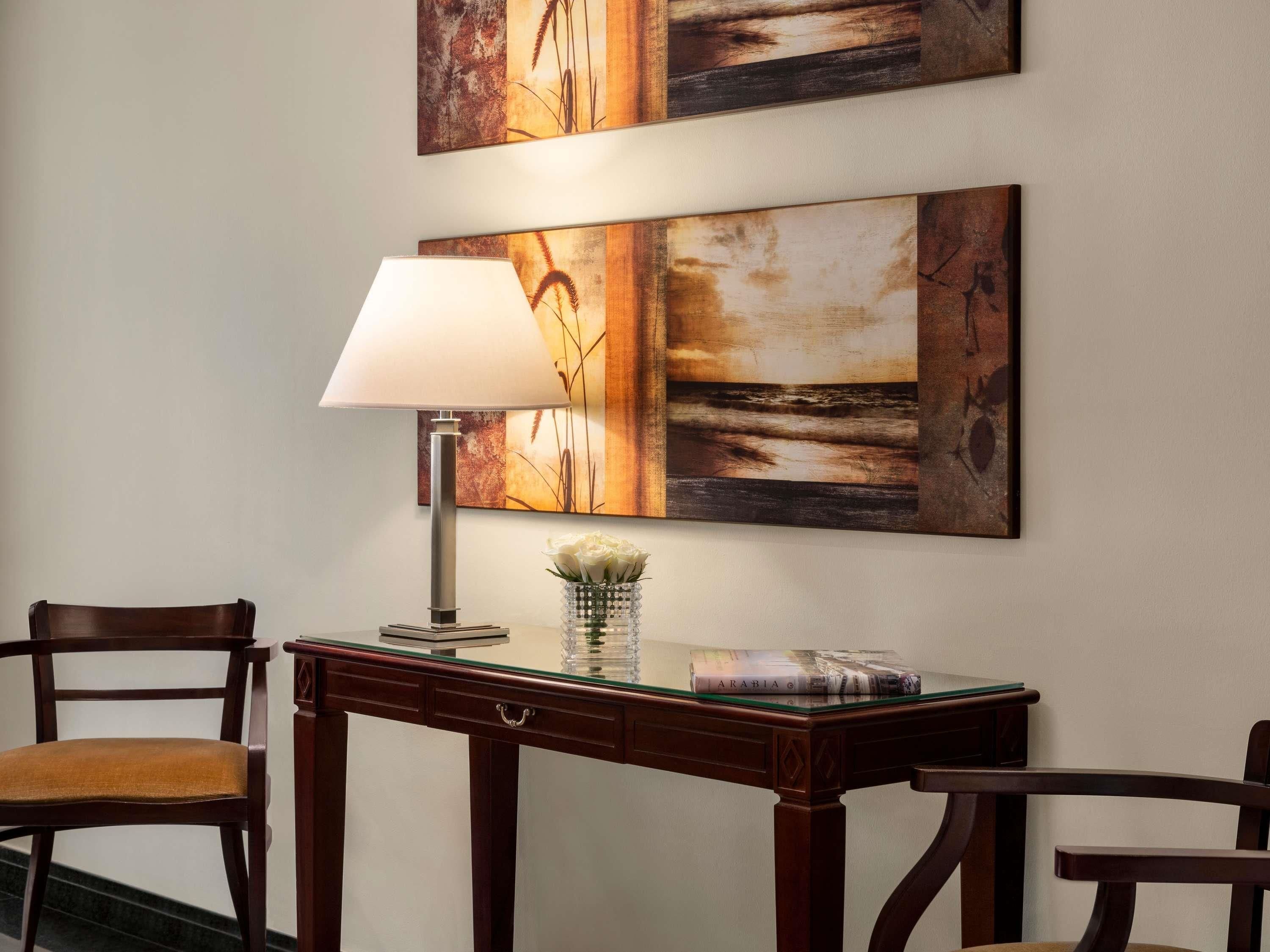A room with a wooden desk, a lamp, and two chairs.