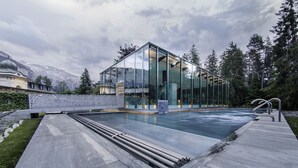 A modern glass building with a pool, surrounded by trees and mountains. - Chalet Belmont Hotel (Flims)