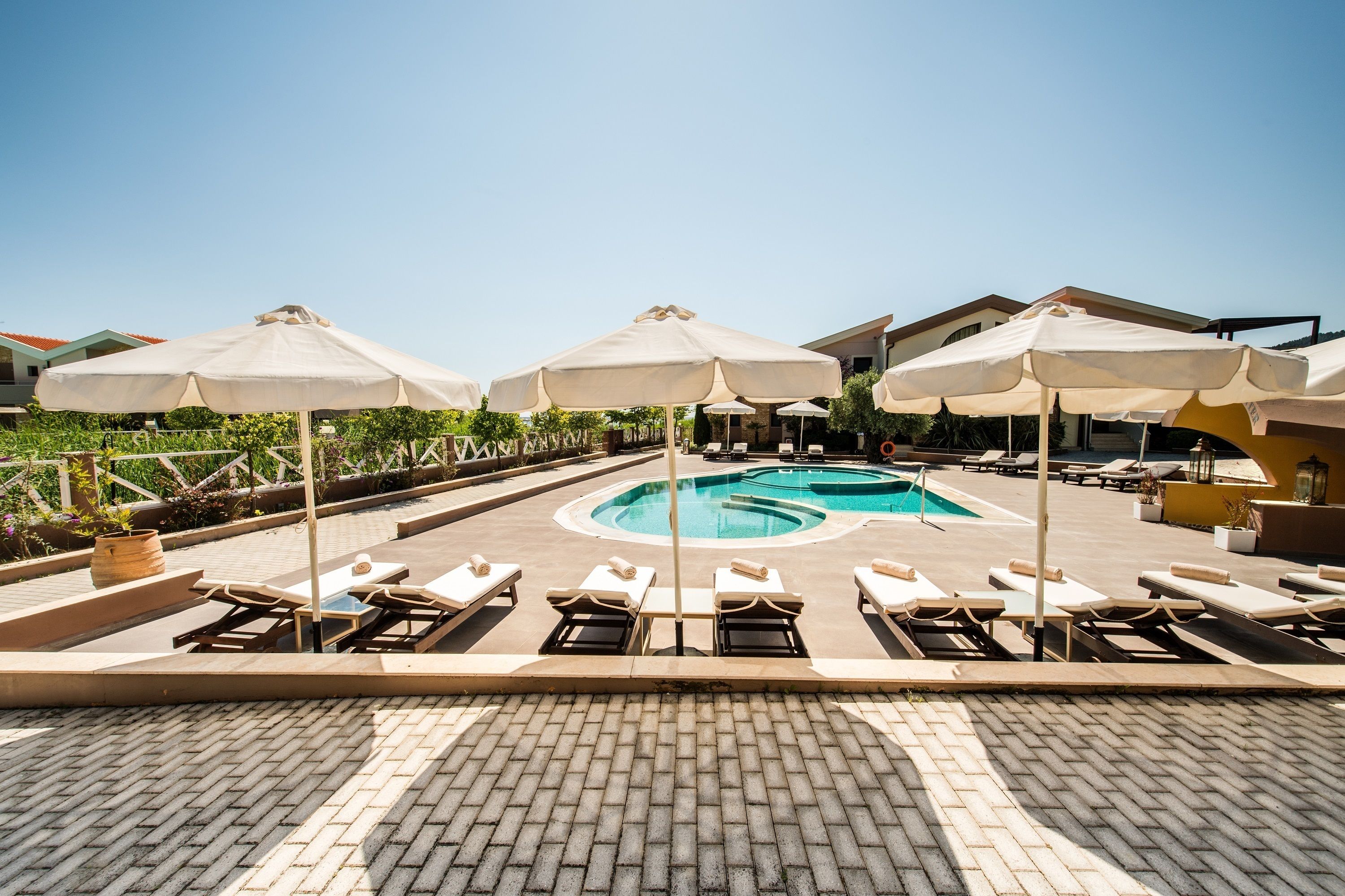 A pool area with lounge chairs and umbrellas, surrounded by a brick patio and greenery.