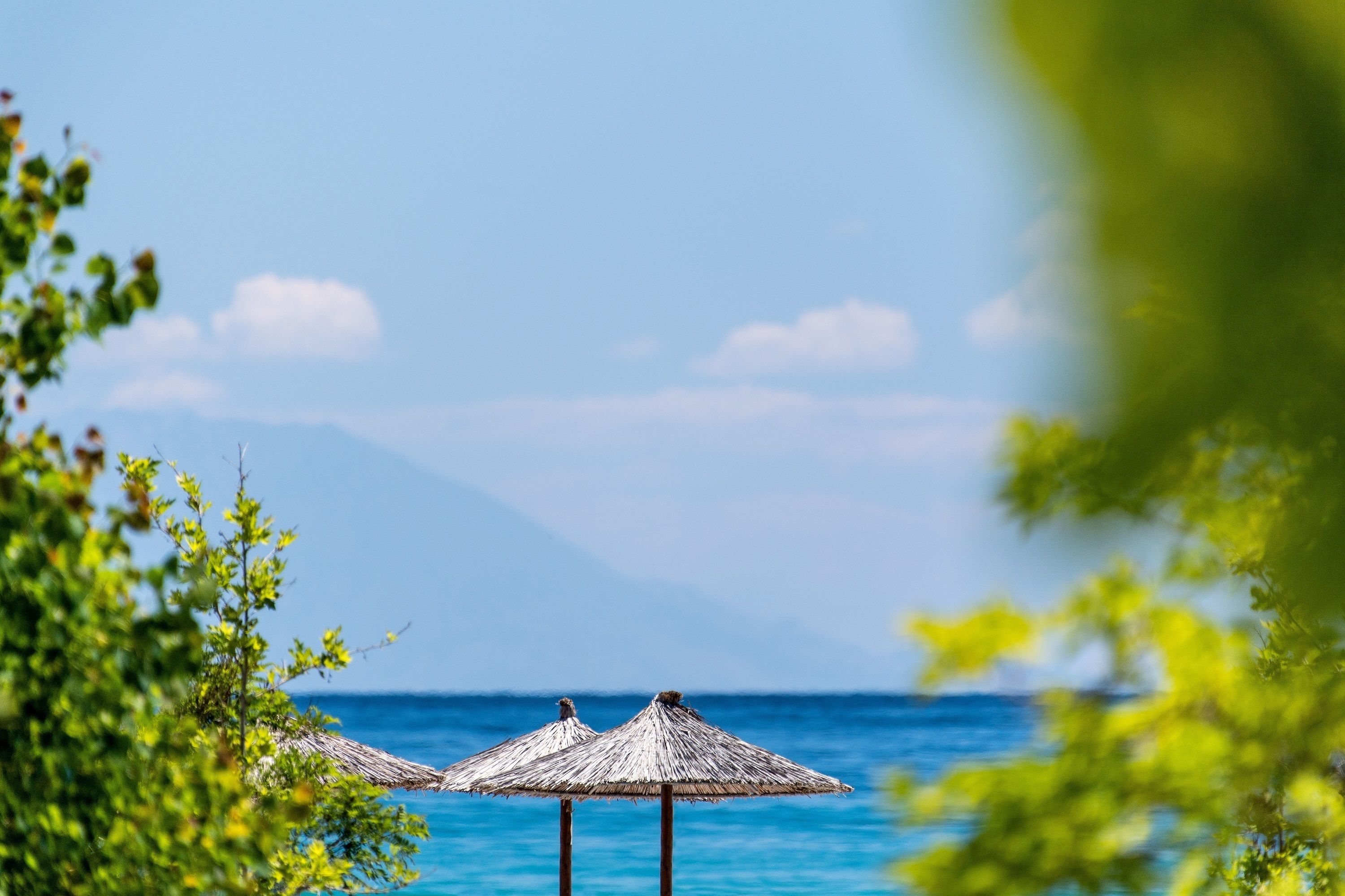 A beach scene with thatched umbrellas and clear blue water.