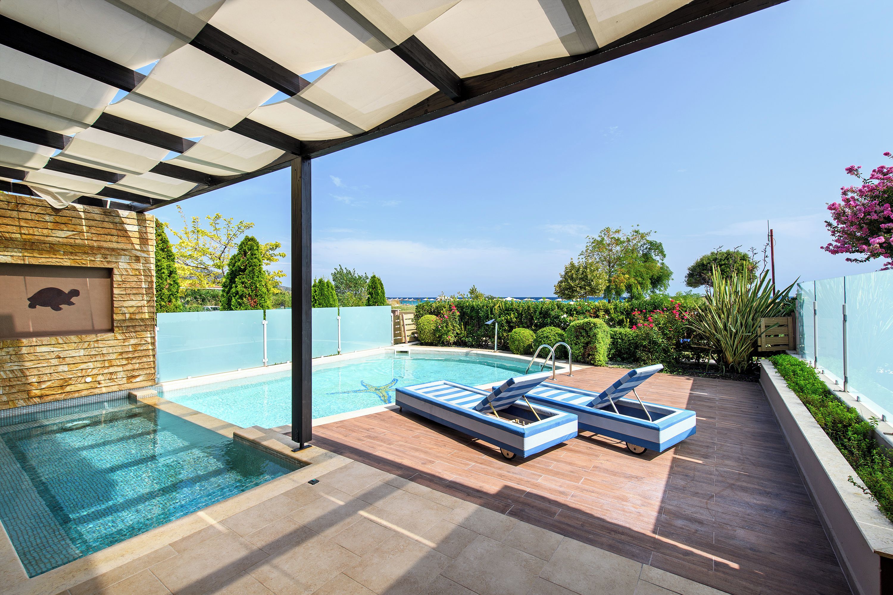 Un espace piscine aménagé sur le toit, offrant une vue dégagée sur l’océan, avec des chaises longues et un mur en pierre.