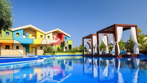 A swimming pool with a wooden gazebo and colorful buildings in the background. - Alexandra Golden Boutique Hotel (Thasos)