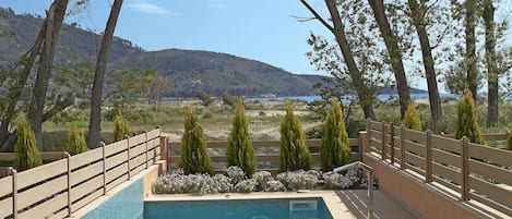 Una piscina con sillas de descanso y una terraza de madera, rodeada de árboles y con vistas a un paisaje montañoso.