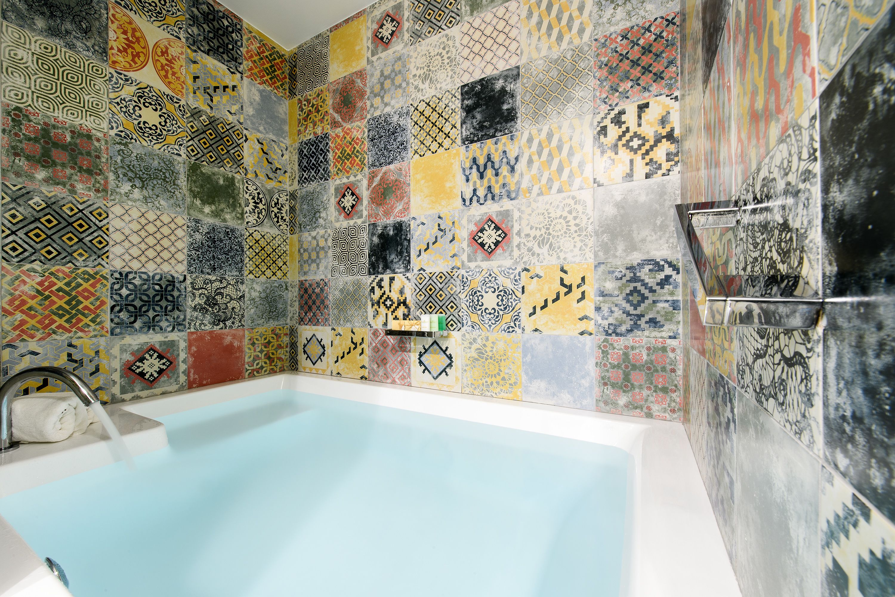 A bathroom with a tiled wall featuring a variety of patterns and a bathtub.