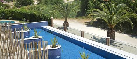 A swimming pool with blue tiles, surrounded by wooden barriers and plants.