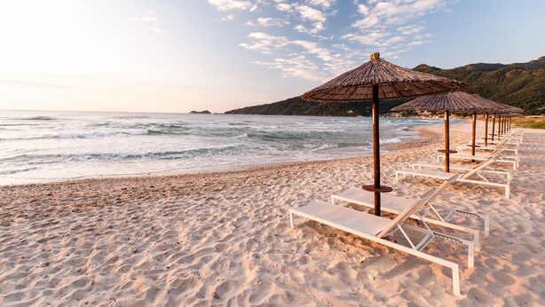 A beach with white lounge chairs and thatched umbrellas. - Alexandra Golden Boutique Hotel (Thasos)
