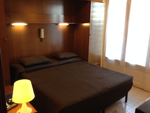 A single bed with a headboard, a bedside lamp, and a window with curtains. - Hotel Nettuno (Diano Marina)