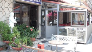 A hotel entrance with a sign reading "Hotel Nettuno," a small outdoor seating area with a table and chairs, and a menu board outside the restaurant. - Hotel Nettuno (Diano Marina)