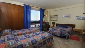 A hotel room with two beds, a window with curtains, a desk, a chair, a small table, and a view of the sea. - Hotel Nettuno (Diano Marina)