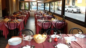 A restaurant with multiple tables set for dining, featuring red tablecloths and metal chairs. - Hotel Nettuno (Diano Marina)