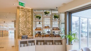 Uma área de recepção de hotel moderna, com um buffet, plantas em vasos e vista para o exterior.