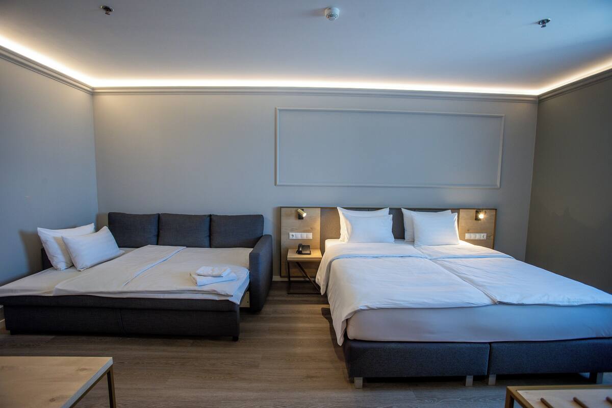 A modern hotel room with two beds, a bedside table with a lamp, and a small table in the corner.