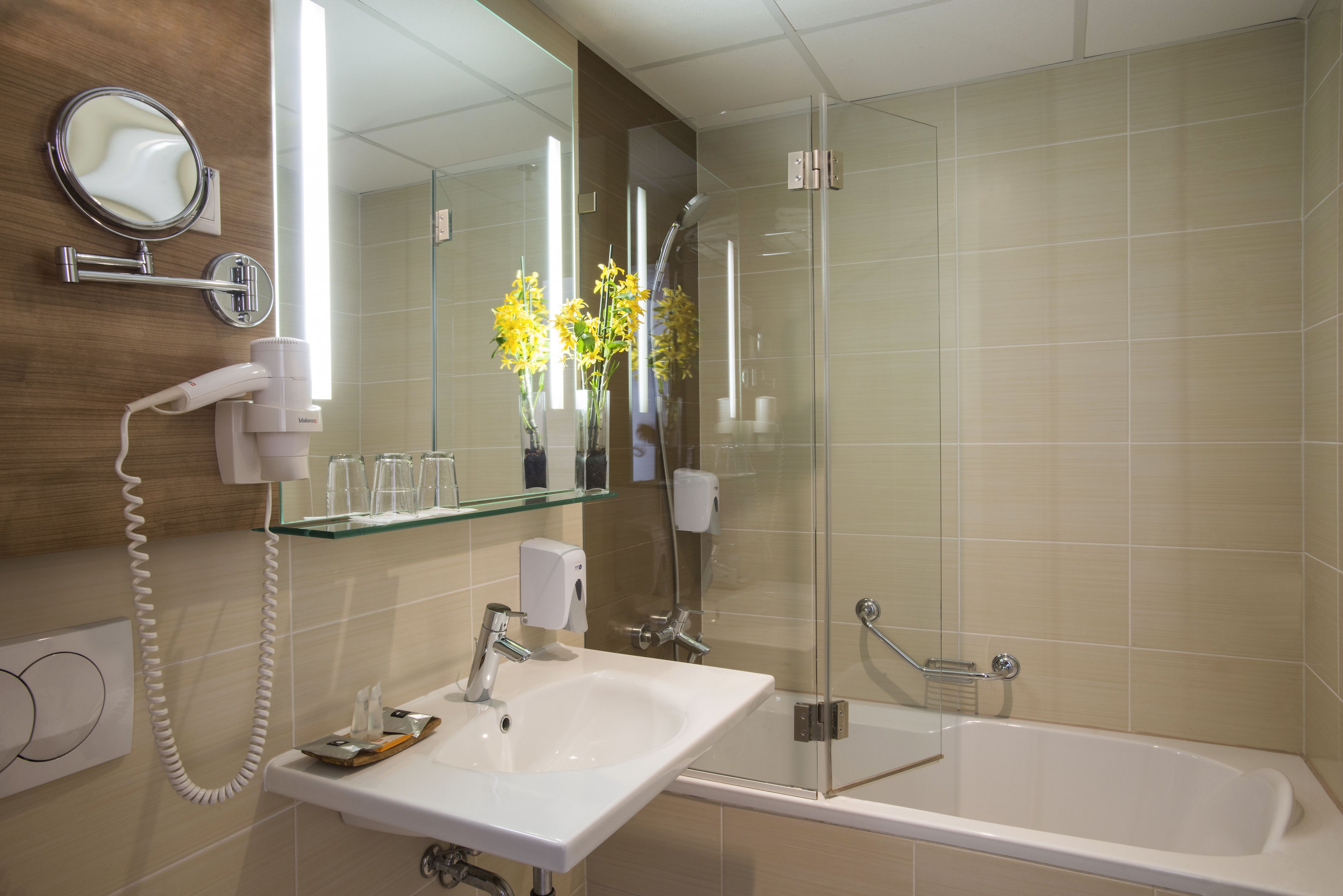 Un baño moderno con un lavamanos blanco, un cerramiento de ducha de vidrio y un secador de pelo de pared.
