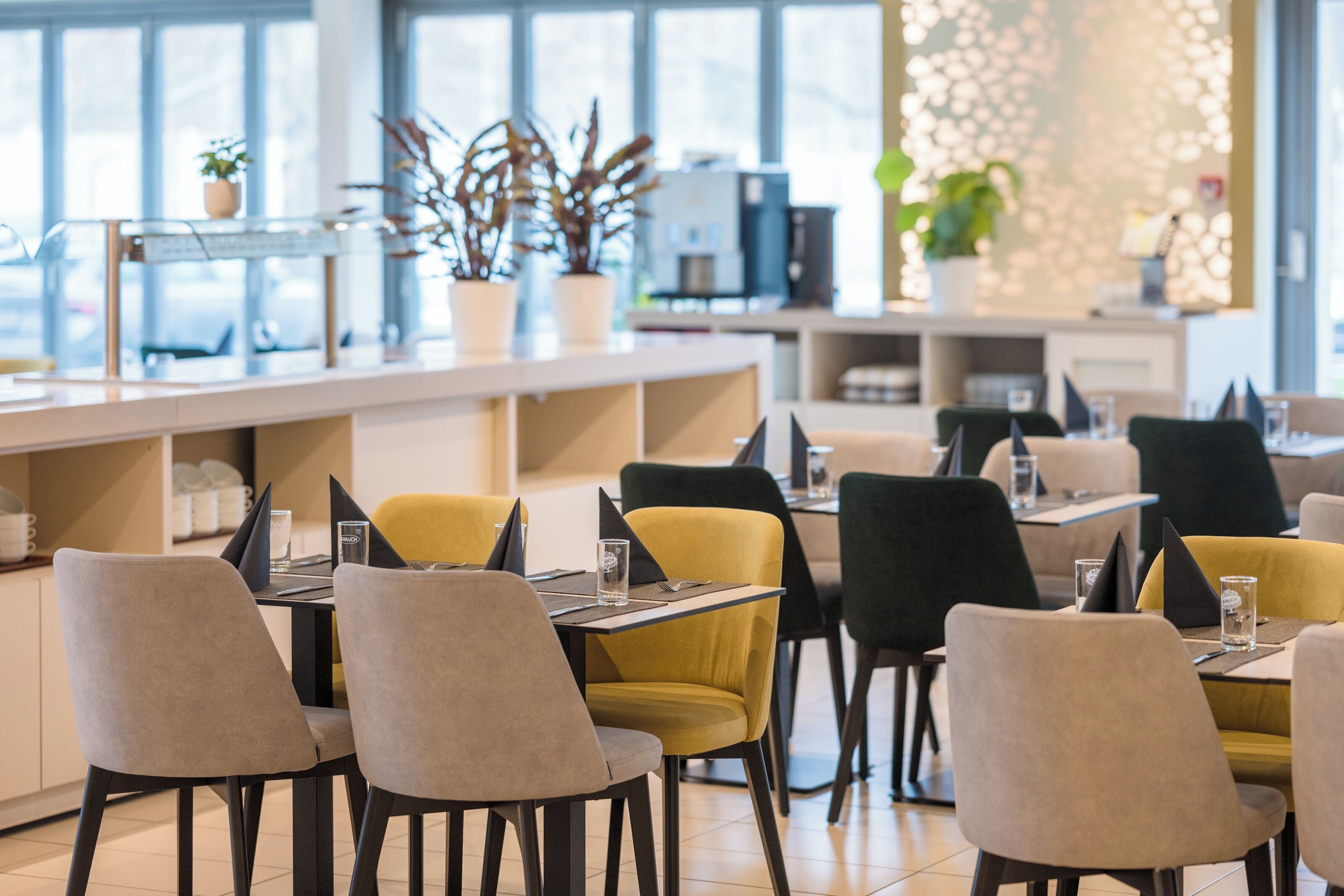 Ένα σύγχρονο εστιατόριο με μπαρ, πολλά τραπέζια με καρέκλες και διακοσμητικά φυτά σε γλάστρες.