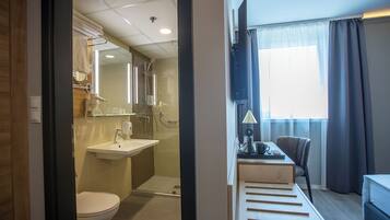 Ein modernes Badezimmer mit Toilette, Waschbecken und Dusche. Über dem Waschbecken befindet sich ein Spiegel, und ein Handtuch hängt an einem Halter. Das Badezimmer hat einen Fliesenboden und ein Fenster mit Vorhängen.