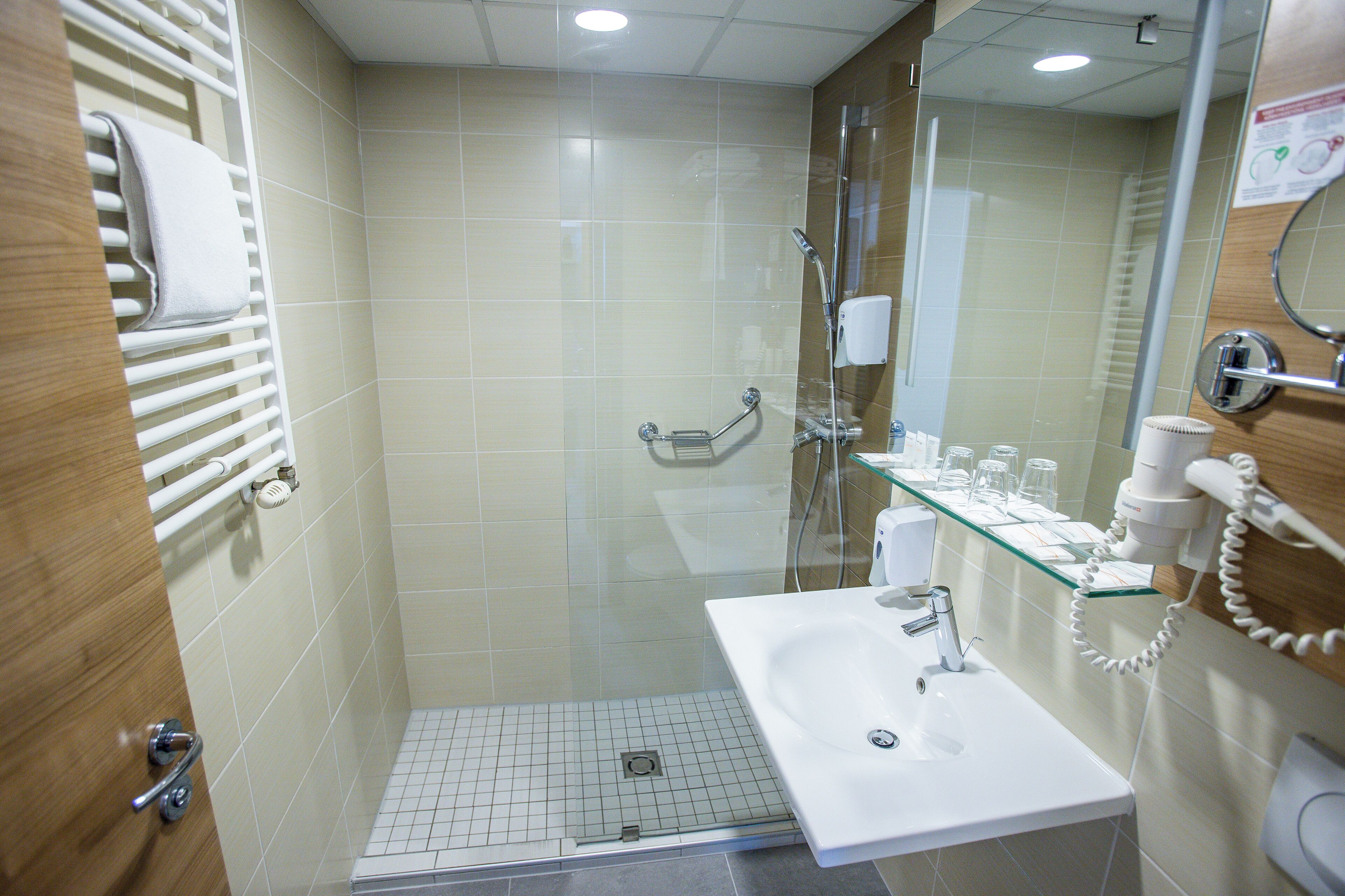 Et moderne badeværelse med et glasbadeværelsesafskærmning, en hvid vask og en glashylde med toiletartikler.
