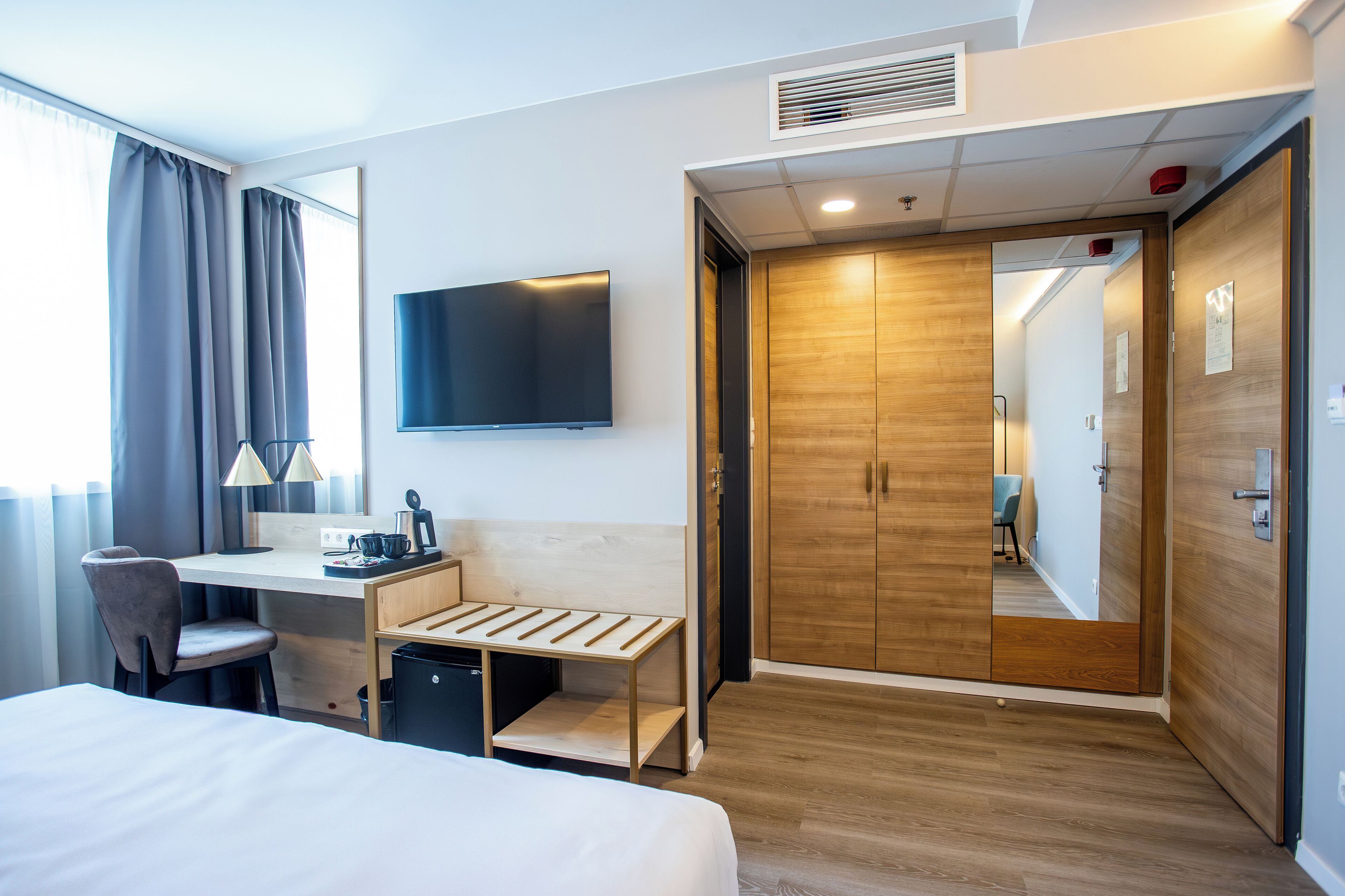 Une chambre d’hôtel équipée d’un lit, d’un bureau, d’une chaise, d’une télévision, d’une armoire et d’une petite poubelle.