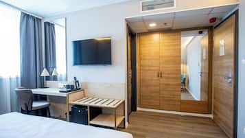 Une chambre d’hôtel équipée d’un lit, d’un bureau, d’une chaise, d’une télévision, d’une armoire et d’une petite poubelle.
