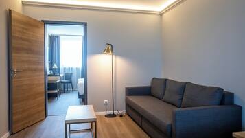 Une chambre d’hôtel moderne avec une porte en bois, un canapé gris, une petite table et un lampadaire.