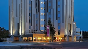 Um hotel moderno com um átrio de vidro, vários andares e um letreiro chamativo com a palavra 'Hotel'.