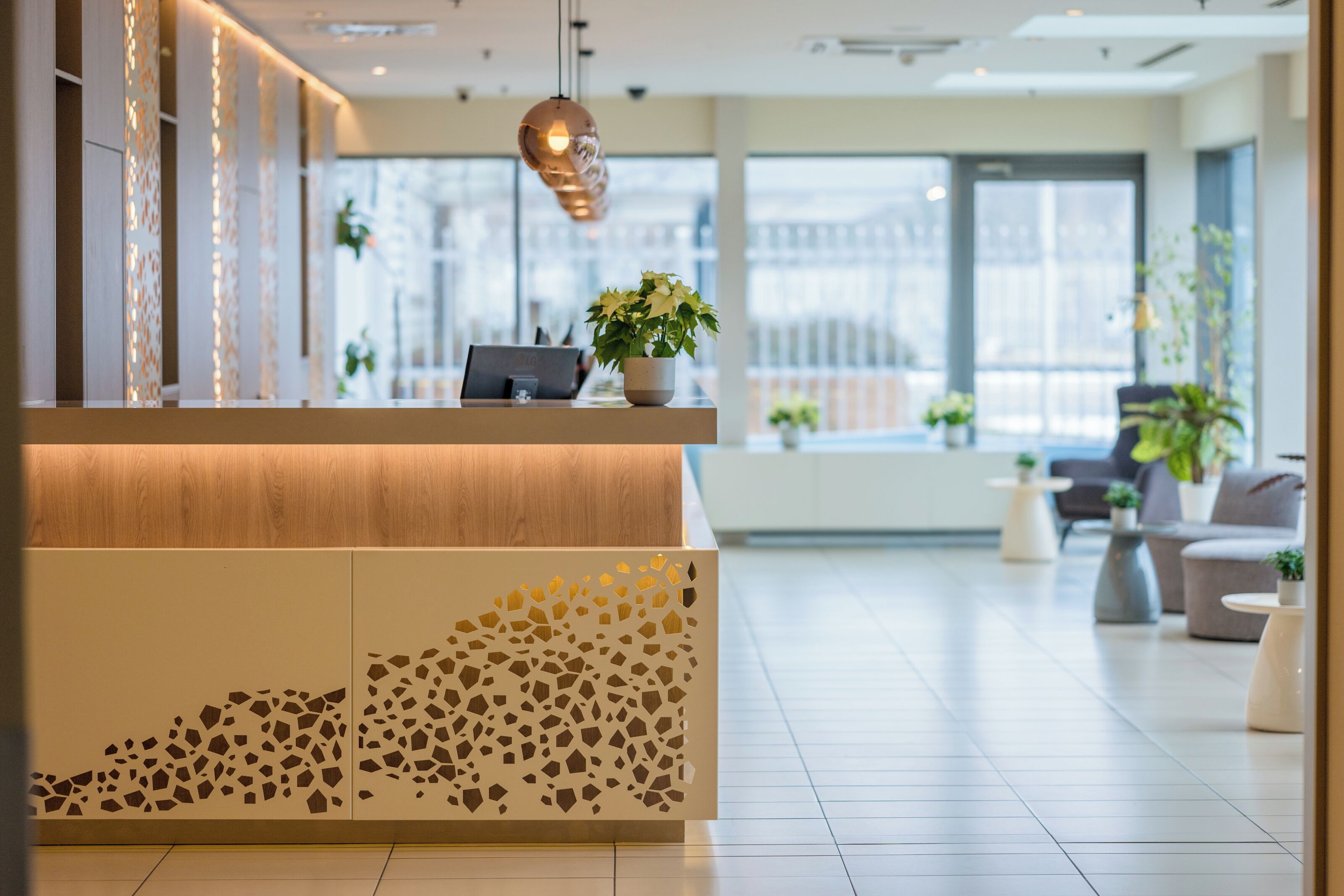 A modern reception area with a wooden reception desk, a potted plant, and a seating area with sofas and tables.