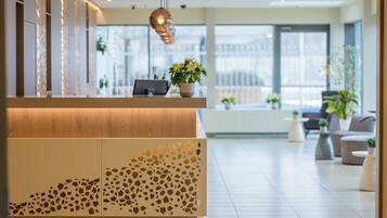 A modern reception area with a wooden reception desk, a potted plant, and a seating area with sofas and tables.